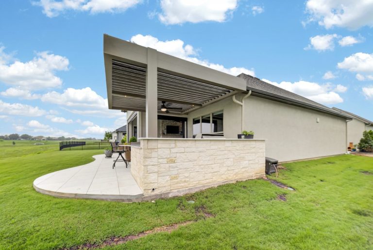 Denton louvered pergola — full roofline and stone kitchen wall with green backdrop